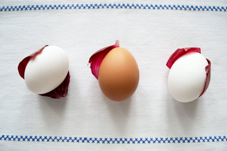 Chicken eggs lying on red onion husks on a white tablecloth with embroidery