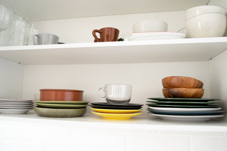 Multicolored dishes on a shelf in a white kitchen cabinet.の写真素材