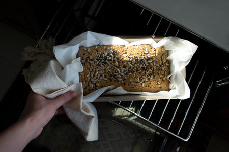 A woman's hand pulls out of the oven homemade bread with sesame and sunflower seeds, fresh baked, rustic loaf of bread. Gluten free baking concept, green buckwheat breadの写真素材