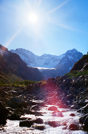 Panoramic view of mountain horizon with glaciers and slopes with trees, mountain natural landscape with mountain river and blue clear sky. Nature of North Ossetia. Film grain effect shotの写真素材