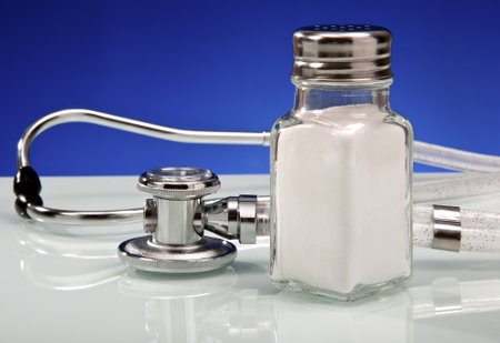 Salt shaker alongside stethoscope demonstrating concept of sodium intake health perception.の写真素材