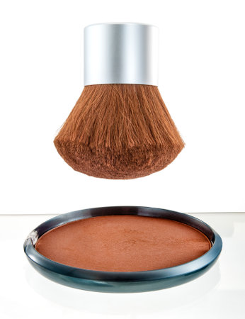 A professional kabuki brush paired with a compact of fine bronzing powder, arranged on a white backdrop. Perfect for makeup, beauty, and skincare representation.の写真素材
