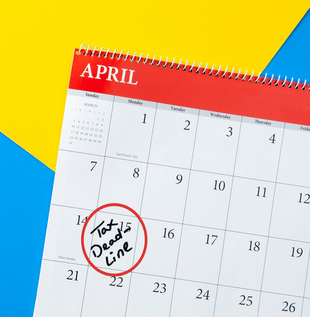 A calendar page for April with a handwritten note marking Tax Deadline on the fifteenth. The image is accompanied by a vibrant yellow and blue background, creating a bright and eye-catching scene.の写真素材