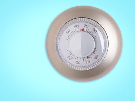 Silver round thermostat on a vibrant blue background. Highlighting energy control, climate adjustment, and interior comfort. A concept for smart home solutions, energy efficiency, and modern indoor technology.の写真素材