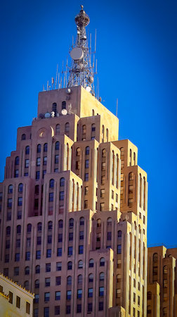 An architectural art deco skyscraper with intricate facades and a distinct mounted radio transmission tower atop, captured during daylight and set against a vivid clear blue background.の写真素材