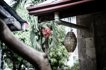 An old lantern is hanging at the water pipe of an old wooden house with a palm tree and dates in the backgroundの写真素材