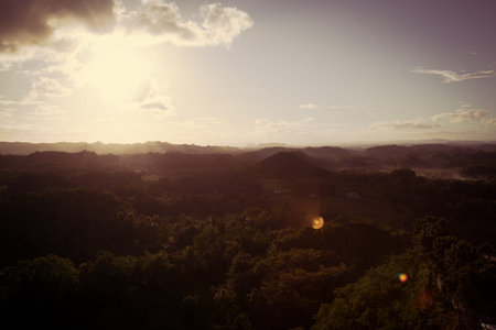 A sunset in Bohol with a slight lens flare and smoke rising in the distance in the green lush jungle of the Philippinesの写真素材