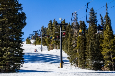 Skiers riding a double chairlift back to the top of the mountain through the trees at a Colorado Ski Resortの写真素材