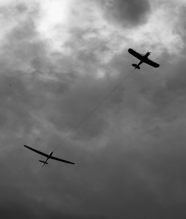 Single engine aircraft flying in a cloudy sky with a glider in towの写真素材