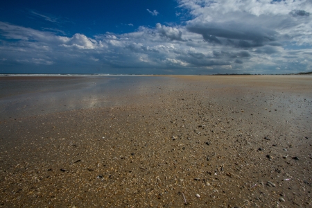 Low persective, wide angle shot of a deserted St  Augustine Beach with blue sky and gray clouds, yellow sandの写真素材