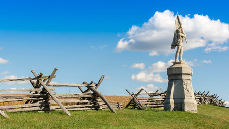 A stone monument of a civil war soldier stands before a wooden split rail fence as it marks the...