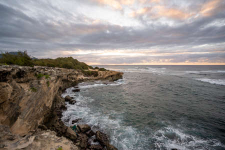 The sun slowly rises over jagged cliffs, which meet the rough turquoise waters of the Pacific Ocean along the Mahaulepu Heritage Trail in Koloa, Hawaii on the island of Kauai.の写真素材