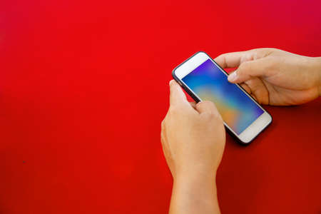 Man hands holding mobile phone on red background with copy space. Flat lay. Top view.の写真素材