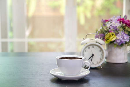 Cups of coffee blurred alarm clock and vase with beautiful flower bouquet  on table in coffee shop background. Space for textの写真素材
