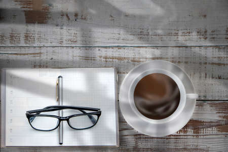 Top view from above of Blank open notebook with eye glasses and coffee on wood table background. Workplace for the creative work of designer at home. Flat lay, Business-finance or education concept with copy space.の写真素材