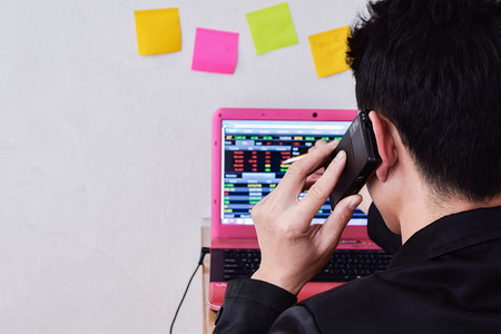 Businessman analysis the stock market on laptop in home office ,focus on hand holding mobile phone for trading , (Concept for Stock Market Investment Online)の写真素材
