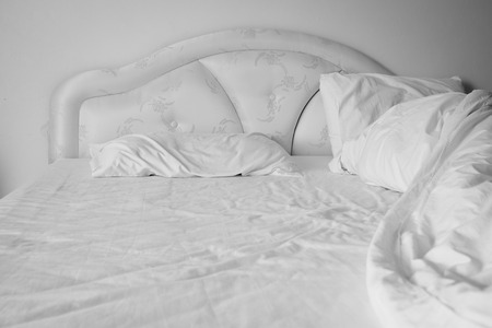 Unmade comfortable bed is strewn with white pillows.(Shallow DOF)の写真素材