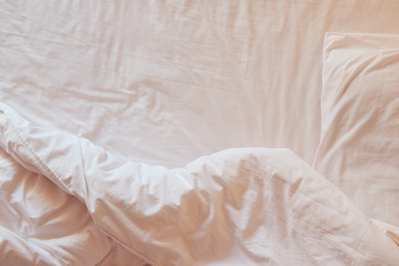 Top view of white bedding sheets and pillow at morning time (soft warm tone)の写真素材