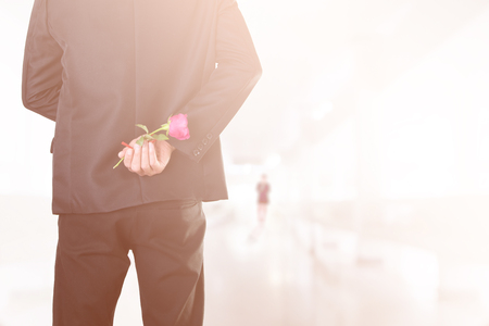 Businessman holding bouquet of roses behind his back with blurred women on path way (soft focus vintage warm tone)の写真素材