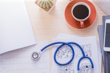 Top view doctor office with cup of coffee,stethoscope, ekg paper and  blank documentの写真素材