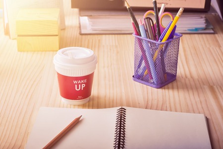 Blank notebook paper with pencil and hot coffee cup with wake up message on office tableの写真素材