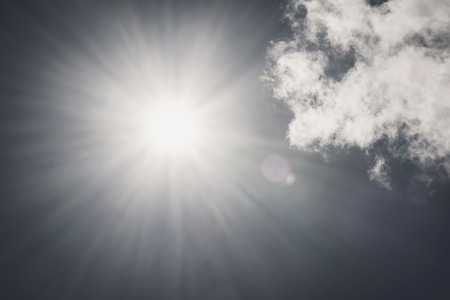 Dark shining sun with lens flare on sky clouds nature day sky background vintage toneの写真素材