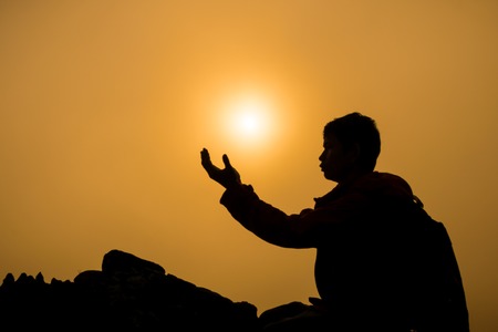 Silhouette of man kneeling and praying over beautiful sunrise on mountain backgroundの写真素材