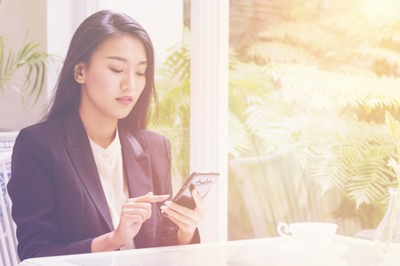 Happy young business woman sitting at urban cafe with coffee ,using her smart phoneの写真素材