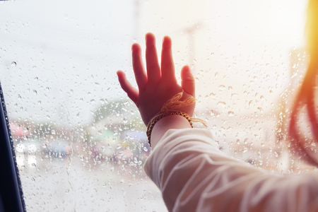 Hand of Little girl looking out of the window with light flare and rain drop on the car door glass, on raining day .の写真素材