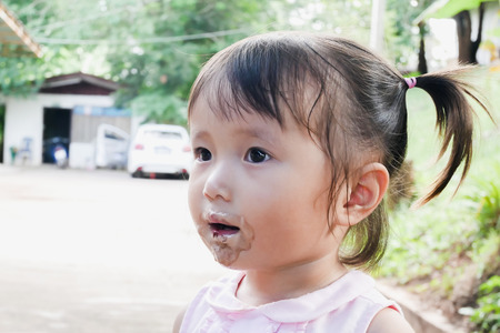 little girl eat ice cream with its mouth smeared with ice cream in park.の写真素材