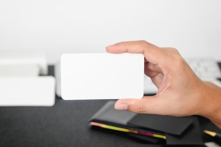 Blank business card mock up in hand on blurre office desk background use us contact information design templete.の写真素材