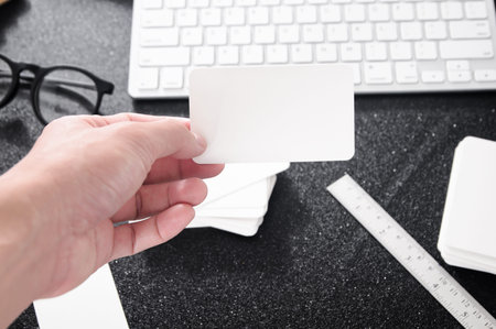Blank business card mock up in hand on blurre office desk background use us contact information design templete.の写真素材
