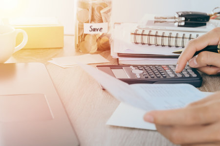 Home Office Expenses concept: Man using calculator on desk with hand holding bank book and coin in...