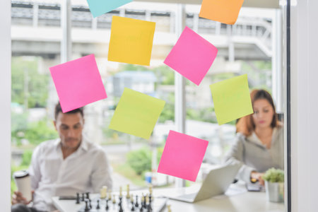 Close up of Post it sticker paper note on glass wall with business people blurred in office