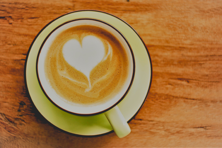 cappuccino hot coffee with foam heart shape on the wooden table backgroundの写真素材