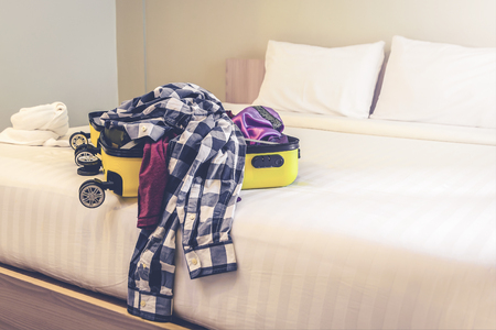 Open travel suitcase with clothes and accessories on bedの写真素材
