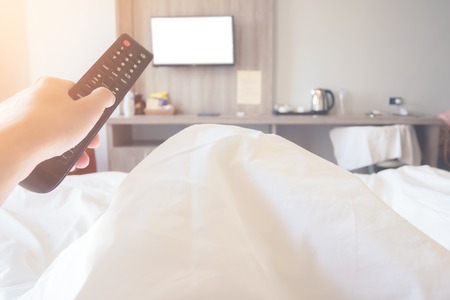 hand holding remote control television ob bed in bedroom close upの写真素材