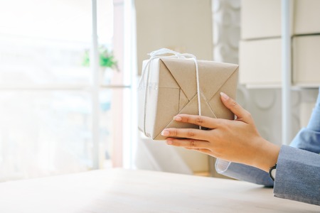 Close up hands holding gift box wrapped with kraft paperの写真素材