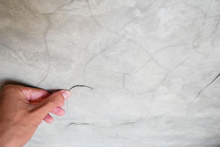 Hand finger pointing to cement cracked wall in house building problems and solutions conceptの写真素材