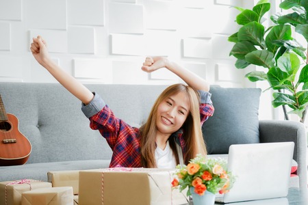 Women smile face with arm raised with the box containing her products to be delivered to customers on desk in the house after video live sells products.の写真素材