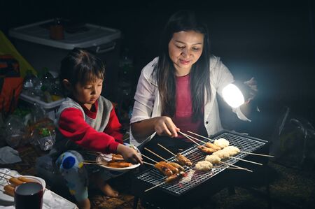 little girl grill meat and hotdogs for dinner, at the camping with mother and familyの写真素材