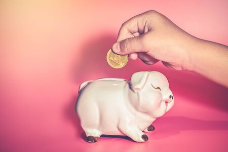 Child's Hand Drop A Coin In Piggy Bank for saving with pile of coins on table at home,Save money for future learningの写真素材
