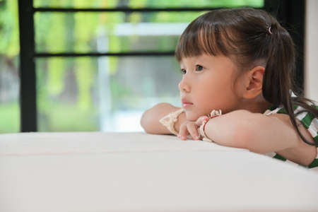 little girl sitting vacant on table feeling empty living without meaning looking forward to no point ,she sad brooded over the bullying done to herの写真素材