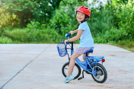 Happy child girl cycling in the park in the village for evening with sunset light exercise. Active child wearing bike helmet. Safety sports leisure with kids conceptの写真素材