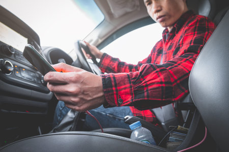 man looking at mobile phone while driving a car his bend down to pick up smartphone on car...