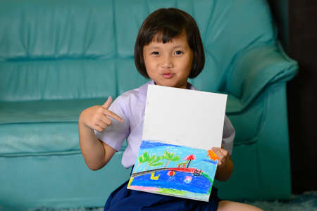 little girl writing and coloring with chalk crayon while relaxing on carpet at home after comeback from schoolの写真素材