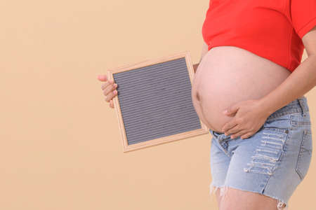 Woman standing and touching with hands her naked big belly,and holding blank board for text pregnancy time - 38 weeks. Baby expectation. happy and safety concept isolationの写真素材