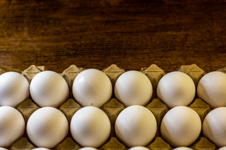 White eggs in a carton box on a wooden background. Top view.の写真素材