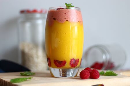 Glass with tasty mango smoothie and raspberry ice cream on wooden table.の写真素材