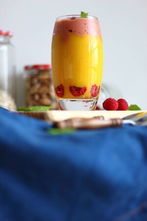 Fresh vegan layered dessert in a glass of colored smoothies of mango and banana with raspberries ice cream, fresh raspberries and mint.の写真素材
